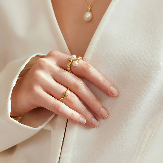 Close-up of a hand wearing gold rings with pearls on a light background